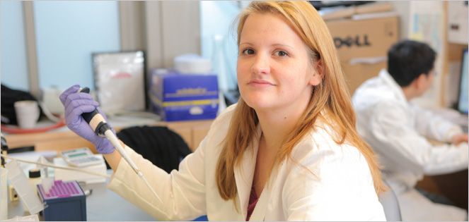 Researcher in a lab coat handles equipment with gloves.